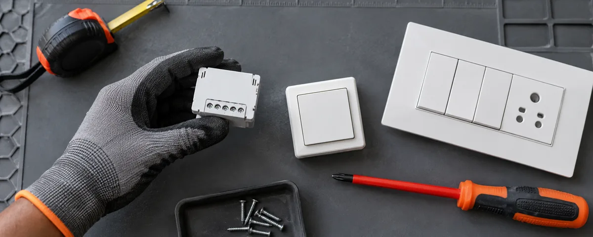 Disconnected relay, wireless button and modular switch plate on a grey electrician’s workbench